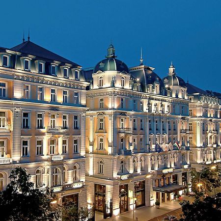 Corinthia Budapest Eksteriør billede The photo shows a large, elegantly designed building illuminated at dusk. It features architectural elements typical of classic European styles, such as ornate detailing, balconies, and a prominent roofline with domes. The facade is beautifully lit, 